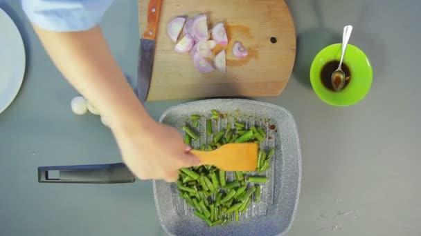 Een vrouw met een houten spatel mengt verse groene bonen in een pan van kokend olie. — Stockvideo