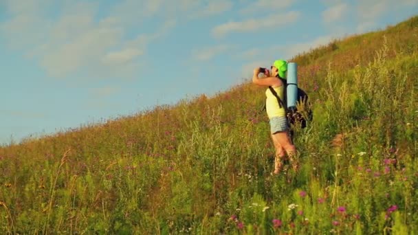 Nő túró a hegyen egy hátizsákot a háta mögött, és távcsövet fényképek jellege a telefon. — Stock videók