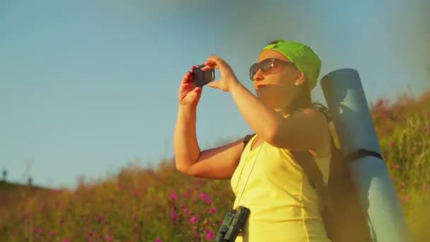 Mujer excursionista en una colina con una mochila sobre sus hombros y prismáticos toma una selfie — Vídeos de Stock