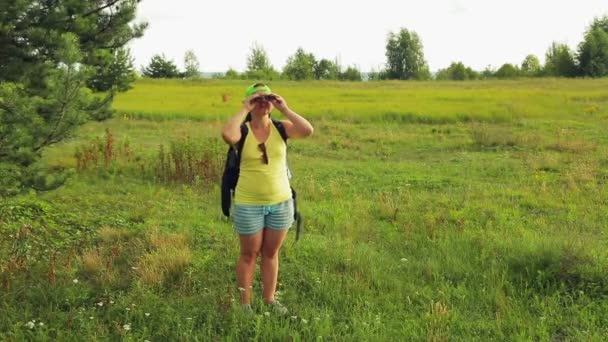 Una turista camina a través de un claro bosque y mira a través de prismáticos a dónde ir a continuación . — Vídeos de Stock