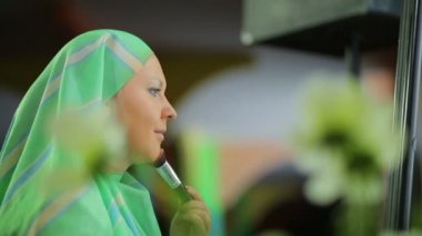 Ayna nın önünde müslüman bir kadın fırçayla bir fondötenle makyaj yapar.