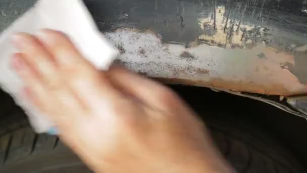 A man cleans rust on the back of a car with emery paper. — Stock Video