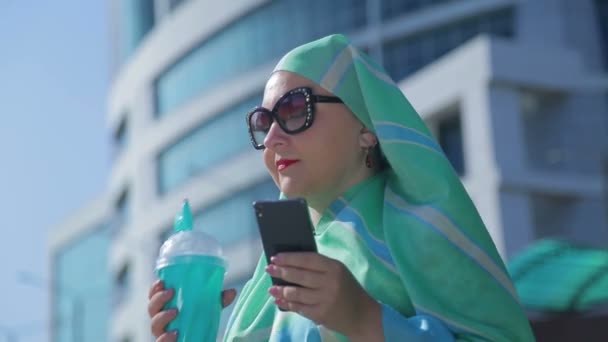 En ung muslimsk kvinna i en lätt halsduk på bakgrunden av en modern byggnad — Stockvideo