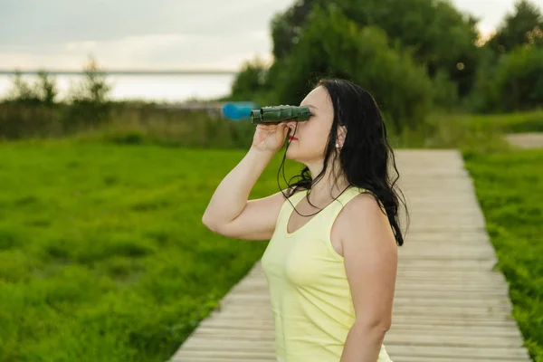 Turista mujer mira a través de prismáticos en la plataforma de observación con vistas al lago . —  Fotos de Stock