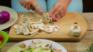 Bir kadın ahşap tahta üzerinde bir bıçak ile dilimleri içine champignon mantar pirzola.
