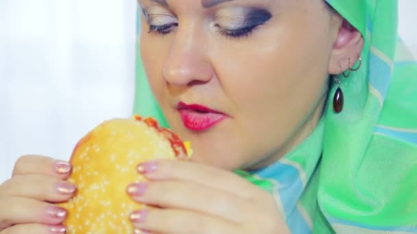 Mladá muslimka ve světle zeleném šálu v kavárně sní hamburger — Stock video