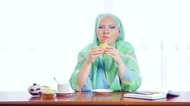 Młoda muzułmańska kobieta w jasnozielonym szalik w kawiarni zjada Burger — Wideo stockowe