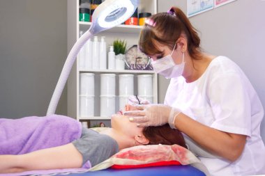 Güzellik salonunda bir güzellik cımbız ile bir müşterinin kaşları ayarlar