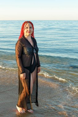 Mayolu genç bir kadın ve Afrika örgülü siyah bir hırka sahil boyunca yürüyor..