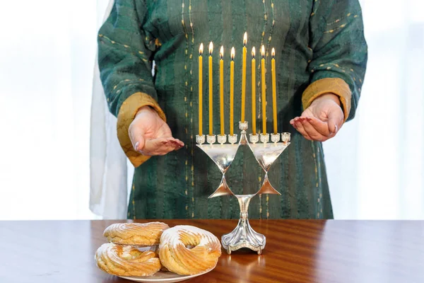 Een Joodse vrouw met haar hoofd bedekt staat aan de feestelijke tafel en Hanukkah lamp. — Stockfoto