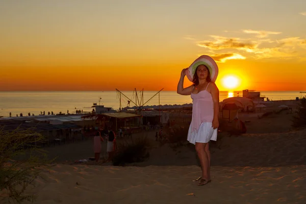 Femme en robe blanche et chapeau de paille sur fond de mer au coucher du soleil. — Photo