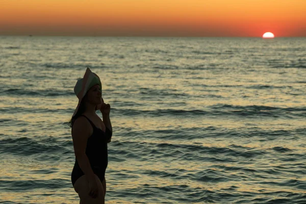 Une femme en chapeau marche le long du littoral au crépuscule . — Photo