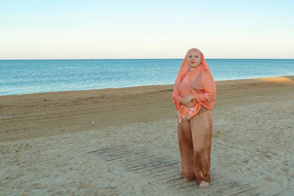 Femme musulmane dans un hijab orange se tient sur le bord de la mer . — Photo