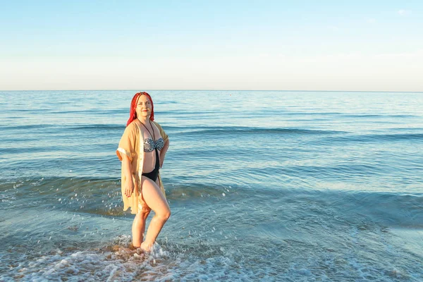 Uma jovem mulher de fato de banho com tranças africanas caminha ao longo da costa . — Fotografia de Stock