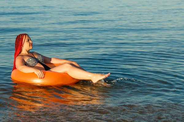 Молодая женщина с африканскими косичками плавает в надувном круге в море возле берега . — стоковое фото