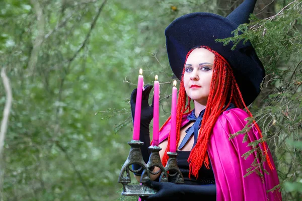 Close-up of a Sorceress in a hat and a purple cloak in a forest in a hand with a burning candle. — Stock Photo, Image