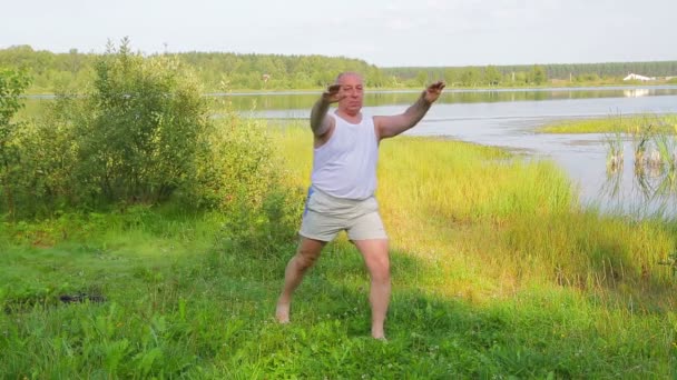 Åldrad man gör stretchingövningar på sjön på morgonen — Stockvideo