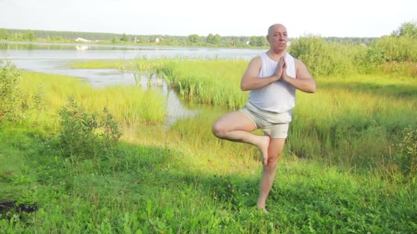 Ηλικιωμένος άνθρωπος κάνει ασκήσεις τέντωμα στη λίμνη το πρωί. — Αρχείο Βίντεο