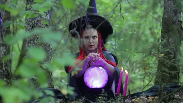 숲에서 빨간 머리를 가진 마법사는 빛나는 공과 불타는 촛불마법을 수행 — 비디오