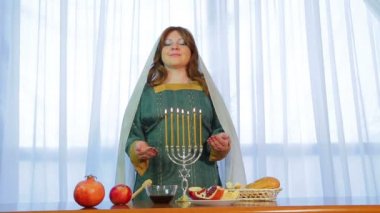 Yahudi bir kadın Rosh Hashanah arifesinde yanan mumlar ile bir festival masada duruyor