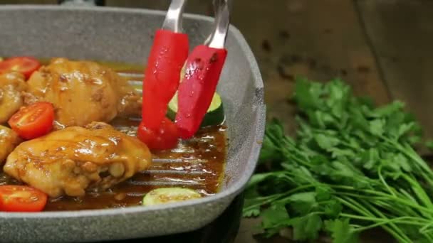 A womans hand turns the pieces of vegetables with forceps and chicken onto a grill pan and pours sauce over it — Stock Video