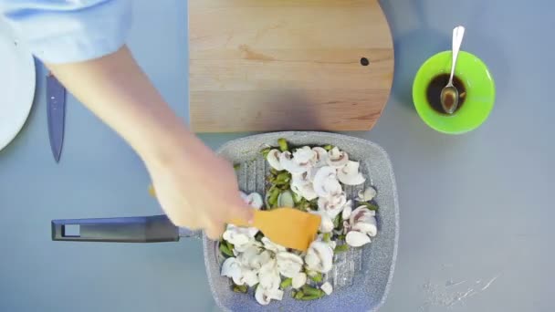 Een vrouw mengt champignons en uien in een pan met een houten spatel. — Stockvideo