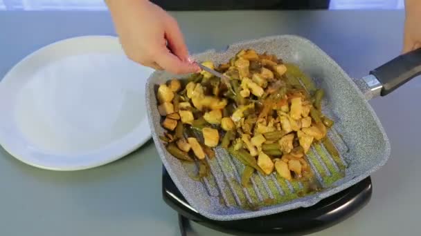 Een vrouw verschuift gebakken kip met groene bonen en champignons uit een koekenpan in een witte plaat. Tijd ronden — Stockvideo