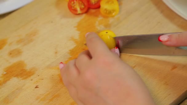 Uma mulher está cortando um tomate cereja amarelo e vermelho com uma faca em uma tábua de madeira. voltas temporais . — Vídeo de Stock