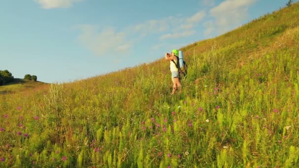 Arkasında bir sırt çantası ve dürbün ile dağda Kadın yürüyüşçü telefonda doğa fotoğrafları. — Stok video