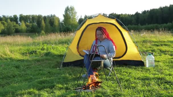 En kvinna nära en halsduk nära en brand läser en bok. — Stockvideo