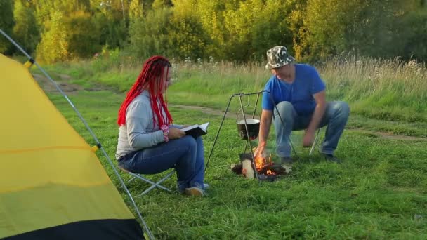 Un homme et une femme près d'une tente près du feu et regarder un chaudron bouillant . — Video