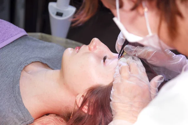 Um esteticista em um salão de beleza arranca sobrancelhas em um rosto de clientes com pinças close-up . — Fotografia de Stock