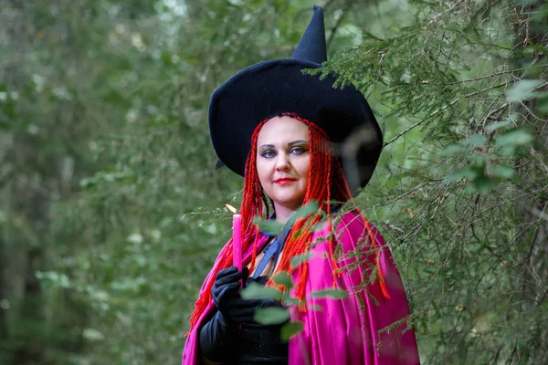 Close-up of a Sorceress in a hat and a purple cloak in a forest in a hand with a burning candle. — Stock Photo, Image