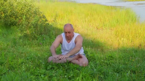 Пожилой человек делает упражнения на озере утром — стоковое видео