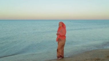 Turuncu şal genç bir Müslüman kadın deniz kıyısında yalınayak yürüyor