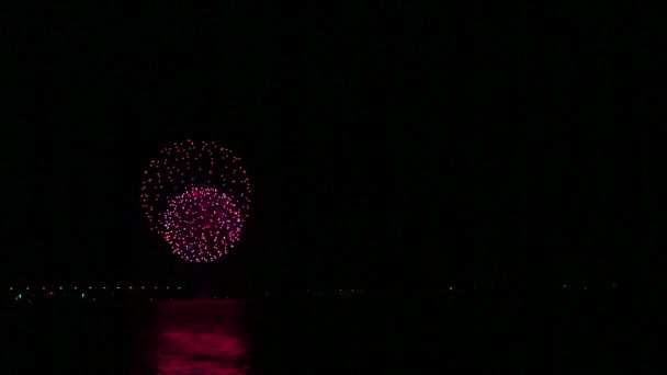 Een kleurrijke verstrooiing van feestelijk vuurwerk in de nachtelijke hemel boven de rivier wordt weerspiegeld in het water. Tijd ronden — Stockvideo