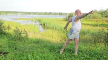 Orta yaşlı bir adam sabahları gölde yoga ve nefes egzersizleri yapar.