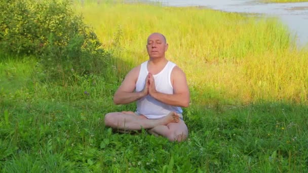 Чоловік середнього віку дихає йогою і медитує на озері вранці . — стокове відео