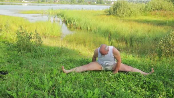 En äldre man gör stretchingövningar på sjön på morgonen — Stockvideo