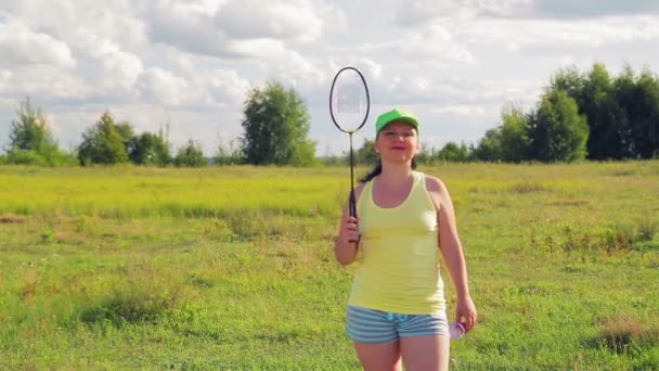 Женщина на лугу дает мяч, когда играет в бадминтон — стоковое видео