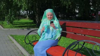 Hafif bir eşarp genç bir Müslüman kadın parkta bir bankta döken ve kahve ve haberci konuşuyor.