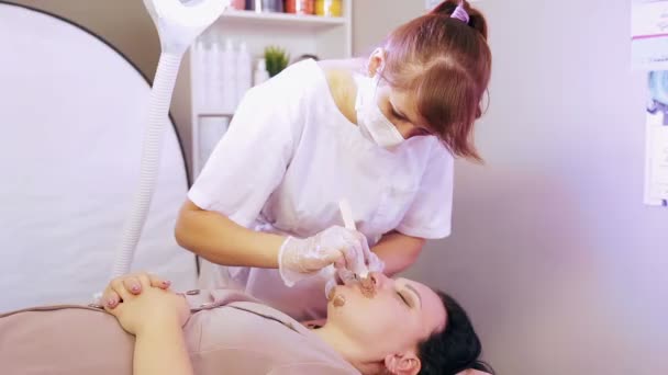 Beauticijník aplikuje horký vosk se stěrkou na tvář vrásky. — Stock video