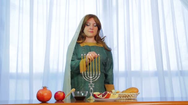 Een Joodse vrouw lichten kaarsen in een mooie kandelaar op Rosh Hashanah op het feestelijke feest met traktaties. — Stockvideo
