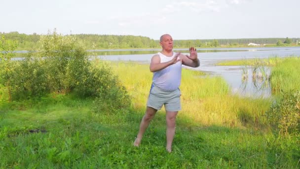 A middle aged man does breathing yoga on the lake in the morning — Stock Video