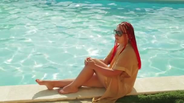 A young woman in a bathrobe and swimsuit is sitting on the edge of the pool. — Stock Video