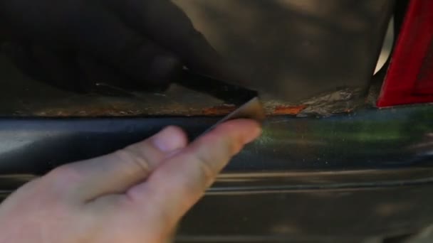 Ένας άνθρωπος καθαρίζει τη σκουριά σε ένα σώμα αυτοκινήτου με μια ξύστρα — Αρχείο Βίντεο