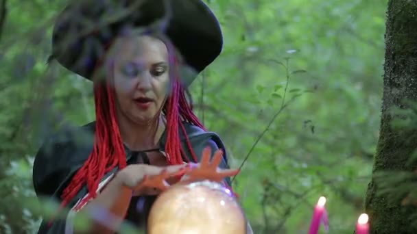 Una hechicera de pelo rojo en el bosque hace magia con una bola luminosa y velas encendidas — Vídeo de stock