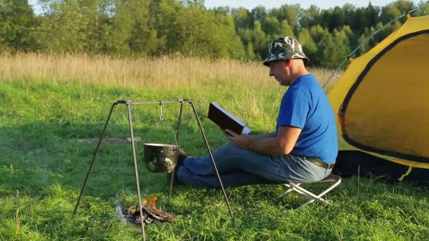 Kamp ateşi çadırına yakın bir adam kaynar tencereyi okuyup izliyor. — Stok video