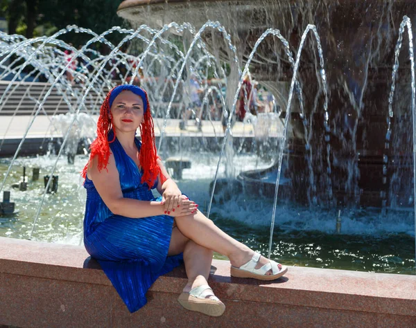 一位身穿蓝色连衣裙、头戴非洲辫子的妇女坐在喷泉的后面. — 图库照片