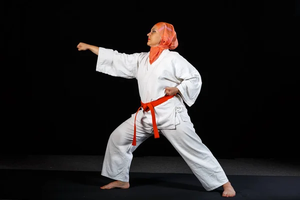 Ung muslimsk kvinna i kimono och sjal under karate träning över svart bakgrund. — Stockfoto